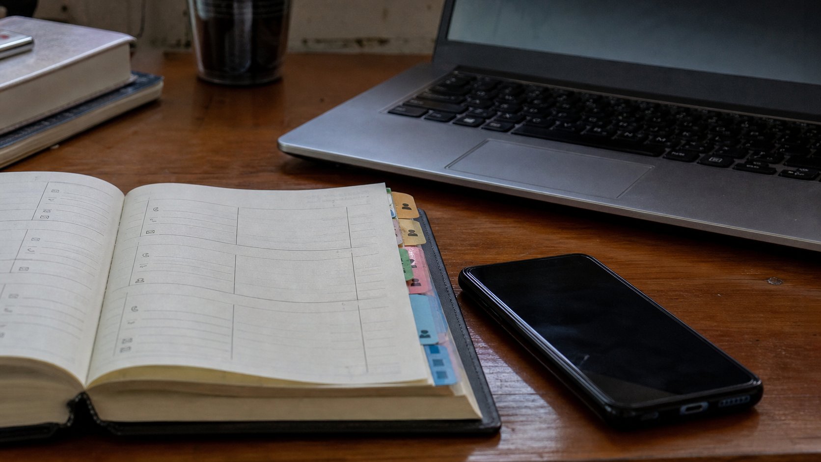 A paper address book beside a phone and a laptop.
