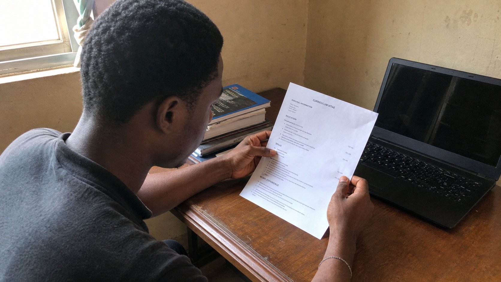 A printed one-page CV beside a laptop, a learner reading it.