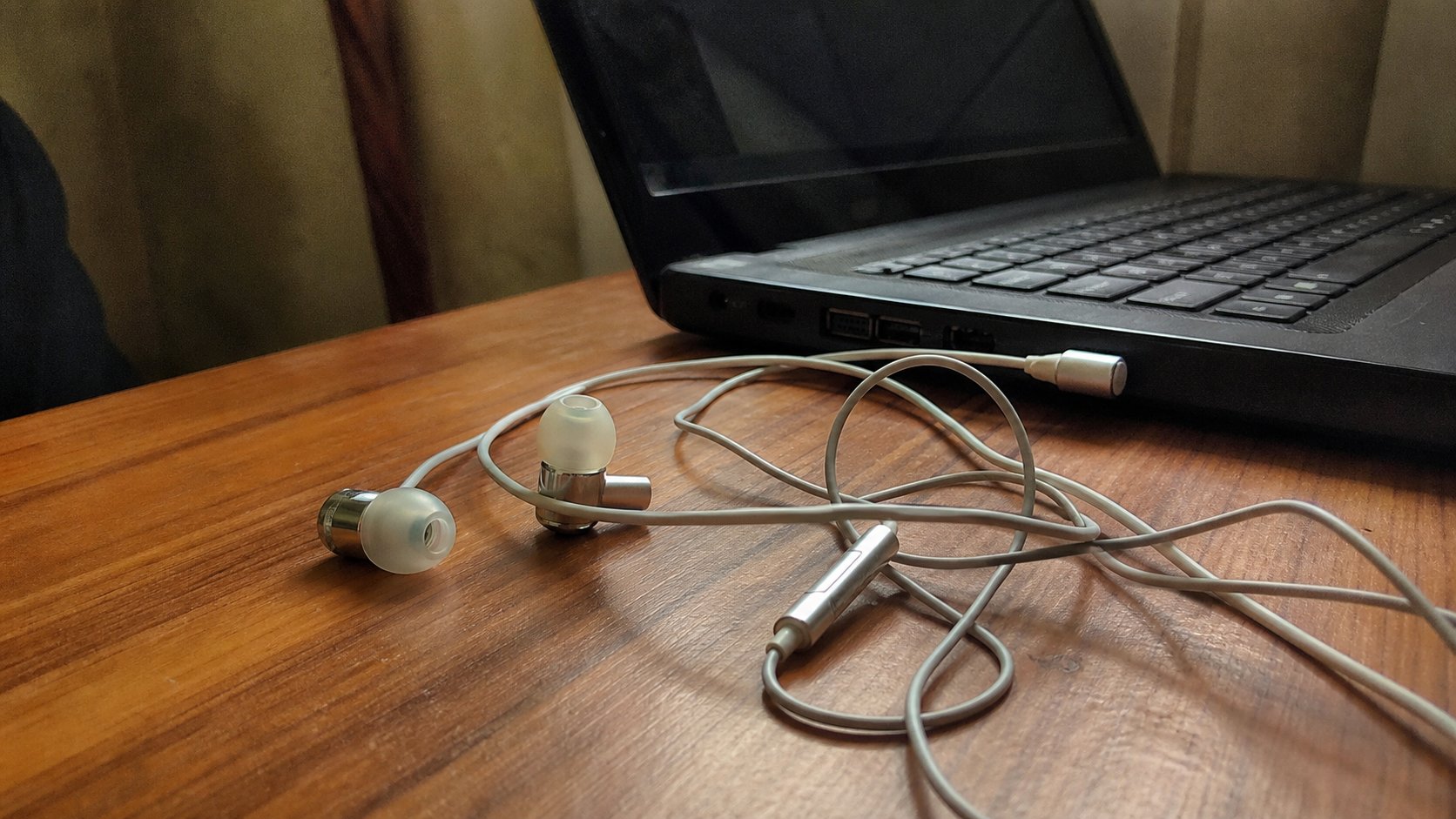 Wired earphones plugged into a laptop on a wooden desk.