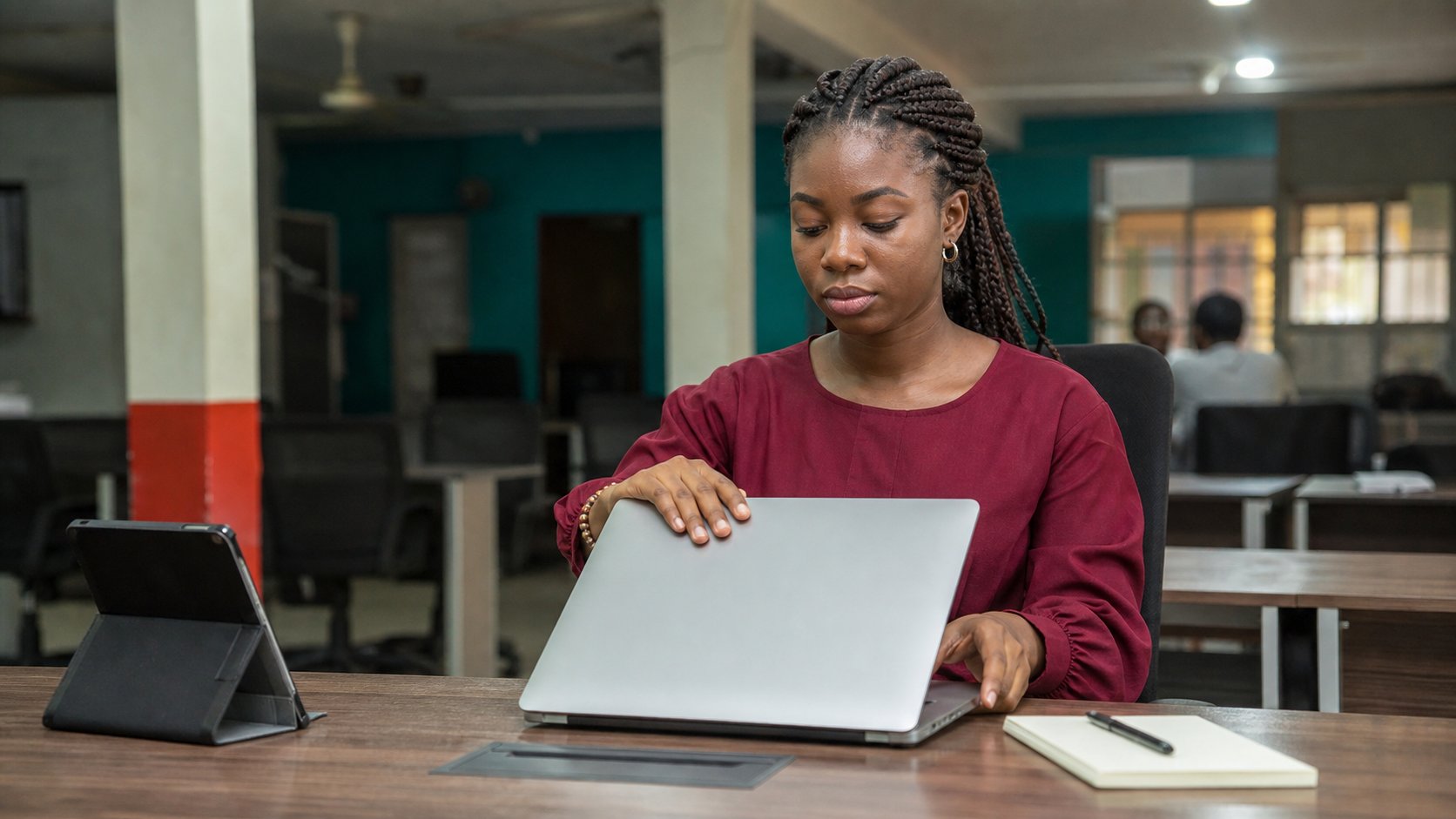 A young woman closing a laptop at a shared desk.