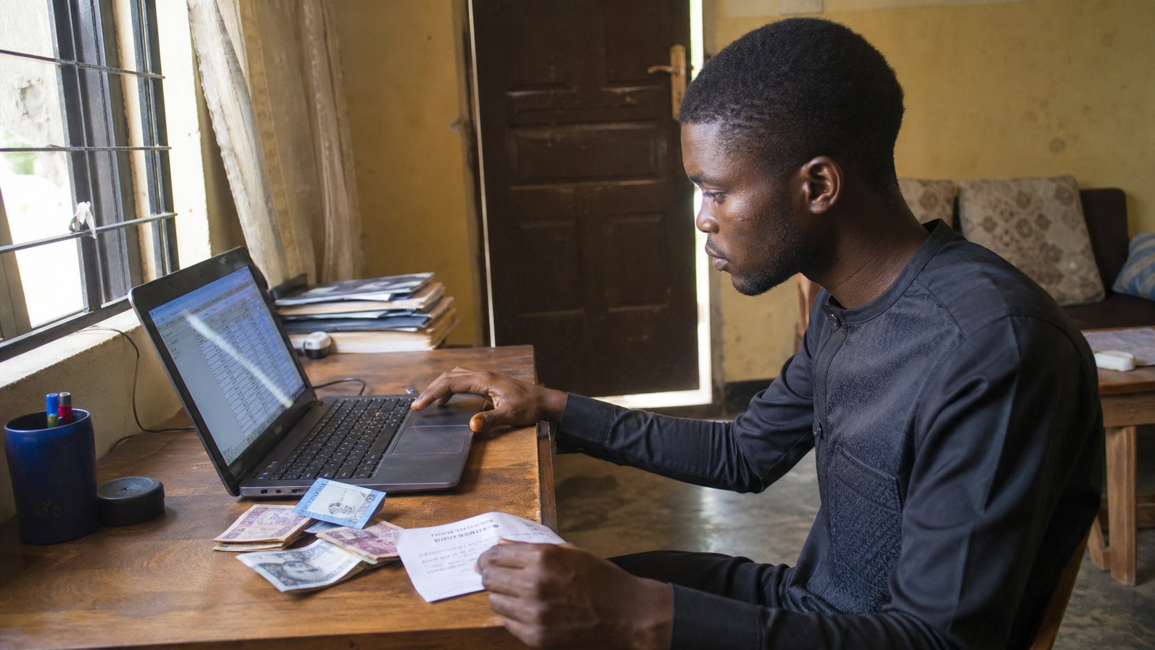 A learner with a spreadsheet of amounts, naira notes and a receipt on the desk.