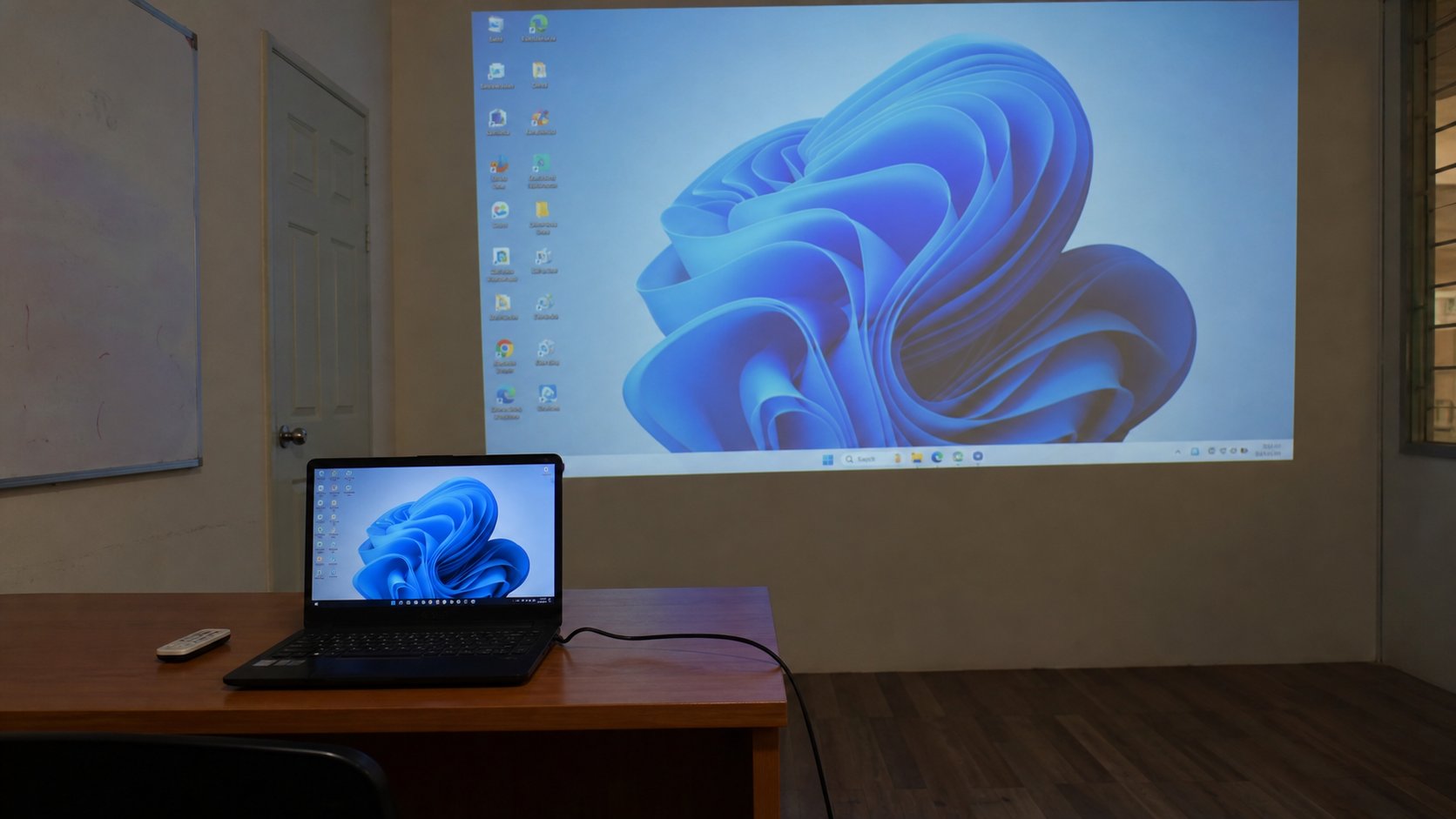 A projector throwing a laptop picture onto a wall, laptop in the foreground.
