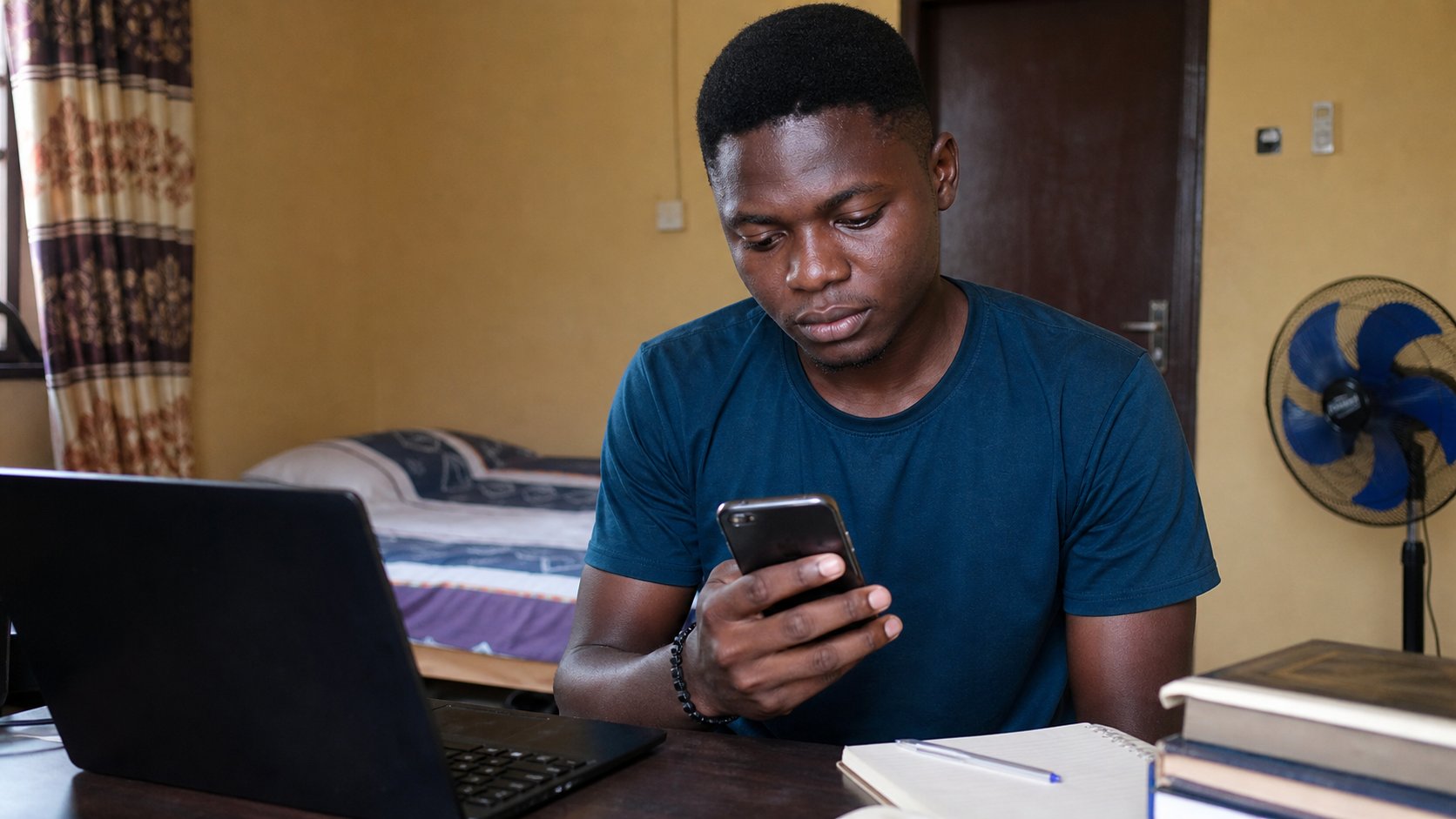 A young man checking a calendar reminder on a phone, laptop beside him.