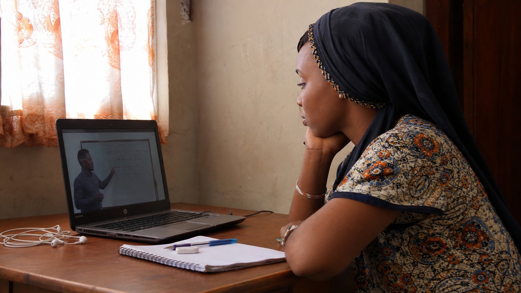 A learner watching a tutorial on a laptop, earphones beside her.